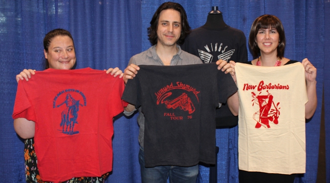 Jason Sprinzen is flanked by his friend Carrie (left, holding a Beach Boys T-shirt) and appraiser Laura Woolley (holding a New Barbarians shirt). Displayed behind them is a Paul McCartney & Wings T-shirt. Sprinzen’s unique collection of 165 rare Showco-branded shirts has a value of more than $70,000. 